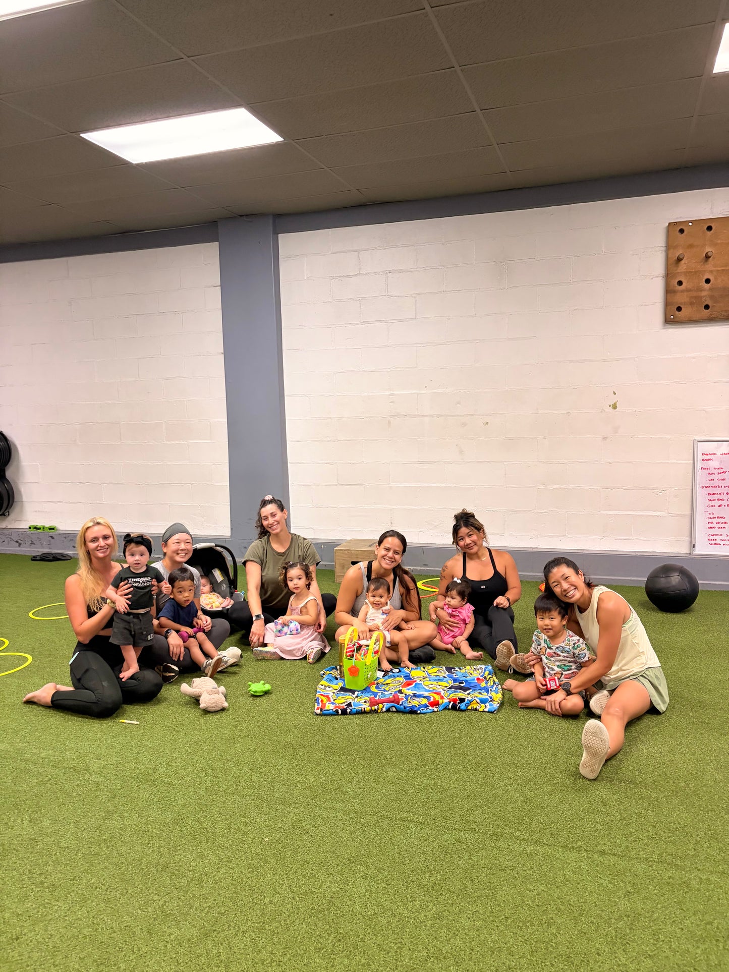 Group of moms and children sitting on a green floor of a gym in Honolulu