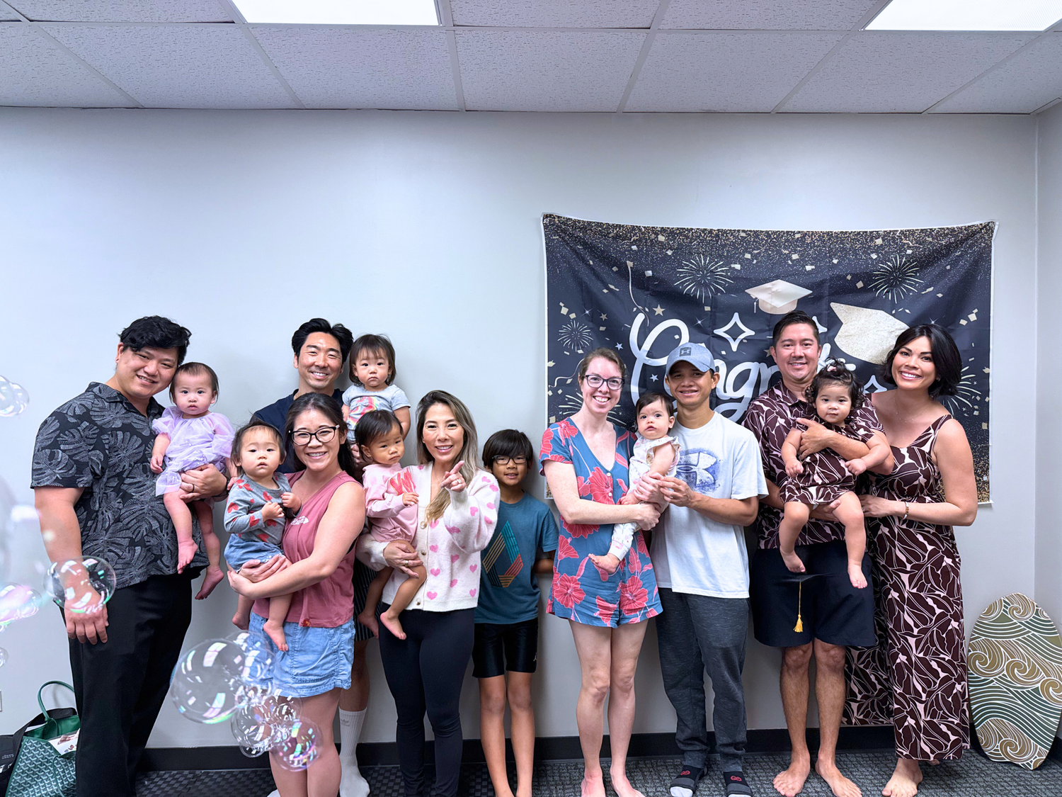 Group of families with babies posing together in a room with a banner in the background