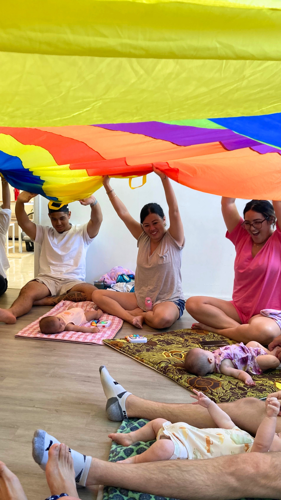 parents with babies under a colorful parachute indoors