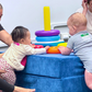 Two babies playing with colorful toys on a blue foam block