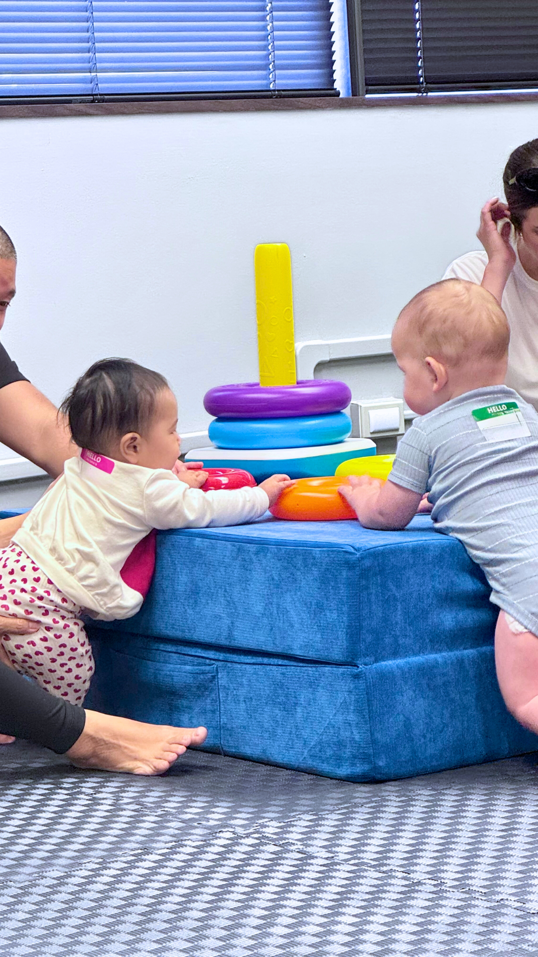 Two babies playing with colorful toys on a blue foam block