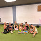 Group of moms and children sitting on a green floor of a gym in Honolulu 