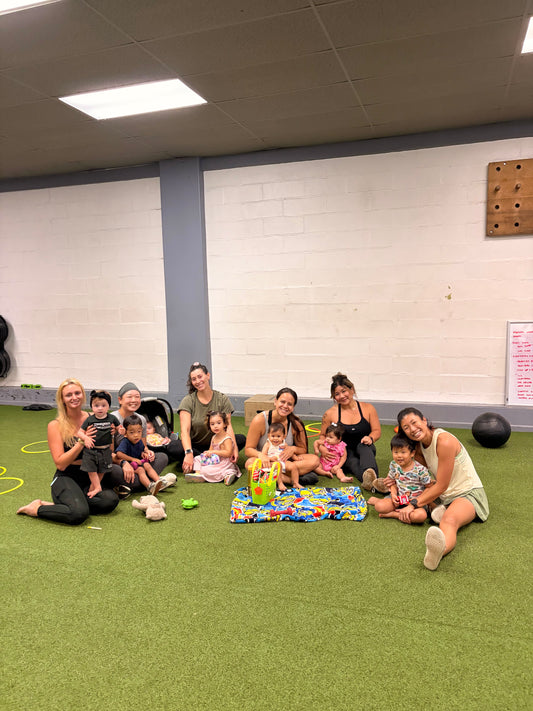 Group of moms and children sitting on a green floor of a gym in Honolulu 