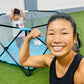 mom flexing her arm muscles in front of a child playing inside a playpen at the gym.
