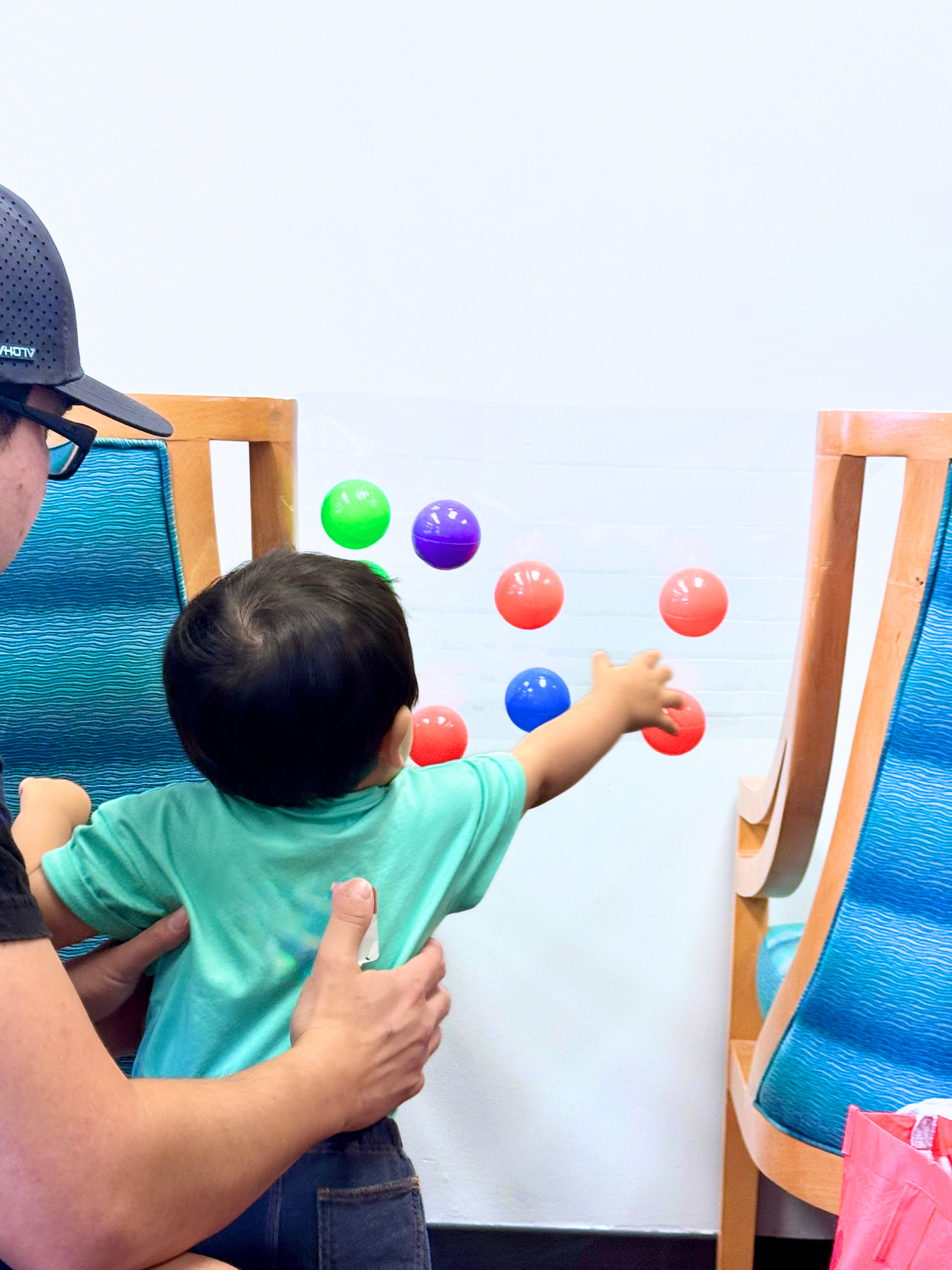 Child and adult playing with colorful balls on a white wall